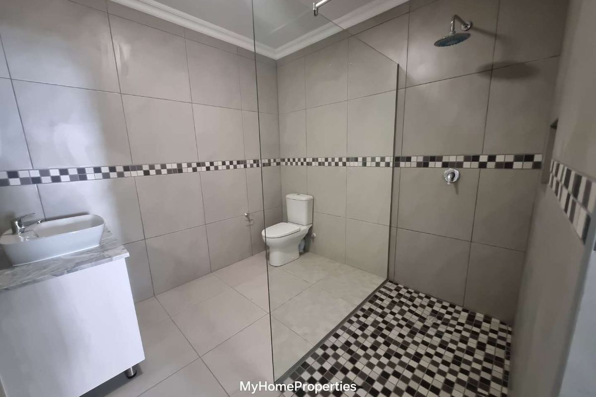 Modern bathroom featuring a spacious walk-in shower with glass screen, contemporary vessel sink vanity, and neutral floor-to-ceiling tiling with decorative mosaic accents.