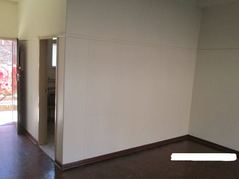 An empty living area featuring dark flooring and plain walls, with an open doorway leading to an adjacent room and exterior access.