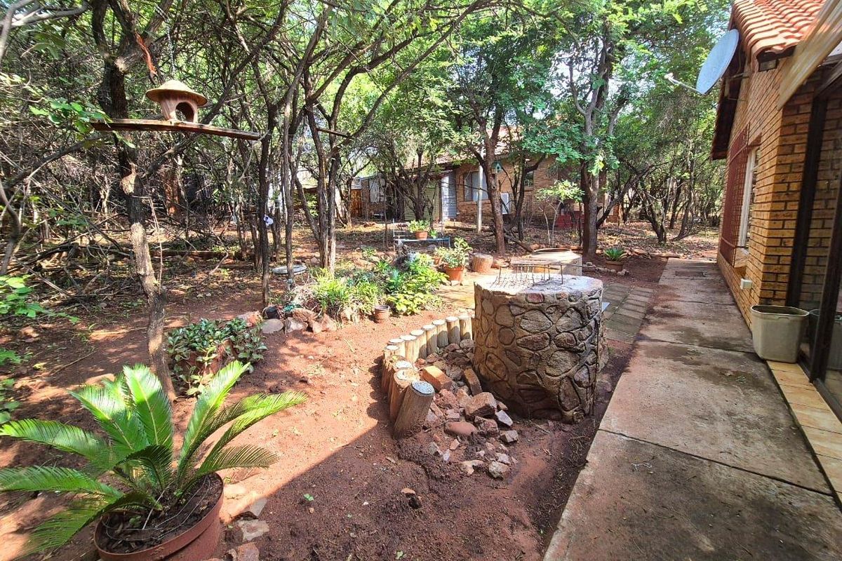 A rustic rear garden area featuring a stone-built braai, paved walkway, and mature trees, offering a natural and private outdoor space.