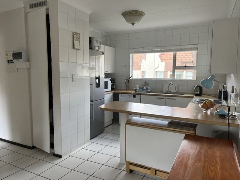 Functional kitchen featuring white tiled walls and flooring, built-in cabinetry, laminate countertops, and a breakfast bar area with integrated hob.