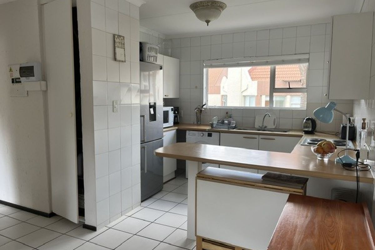 Functional kitchen featuring white tiled walls and flooring, built-in cabinetry, laminate countertops, and a breakfast bar area with integrated hob.