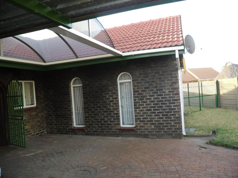 Rear exterior view featuring a brick facade, arched windows with security bars, a paved patio area, and a covered outdoor structure.