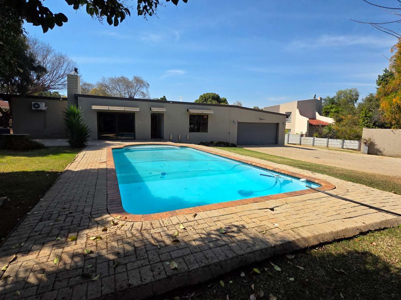 Rear exterior view featuring a swimming pool with paved surround, adjacent garage, and established garden area.