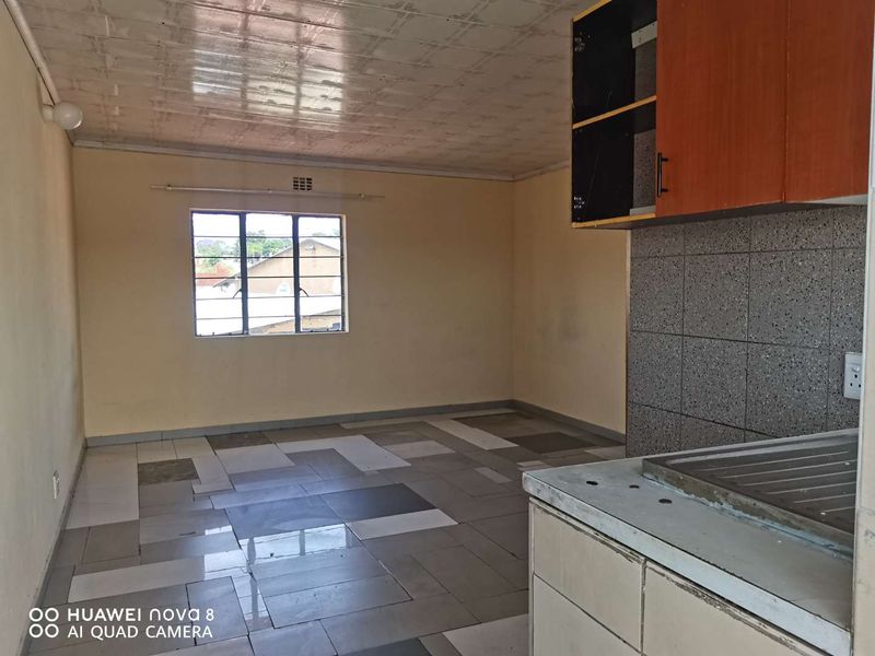 Open plan living and kitchen area featuring tiled flooring, basic cabinetry, and a steel-framed window. The space is vacant and ready for renovation.