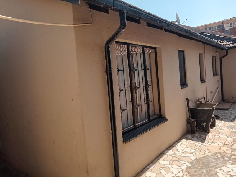 Rear exterior view showing a paved courtyard area with a built-in concrete wash trough and security-barred windows.