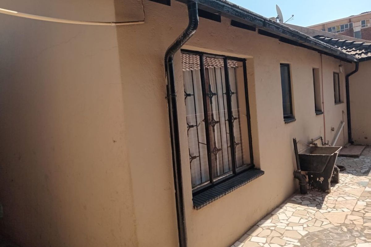 Rear exterior view showing a paved courtyard area with a built-in concrete wash trough and security-barred windows.