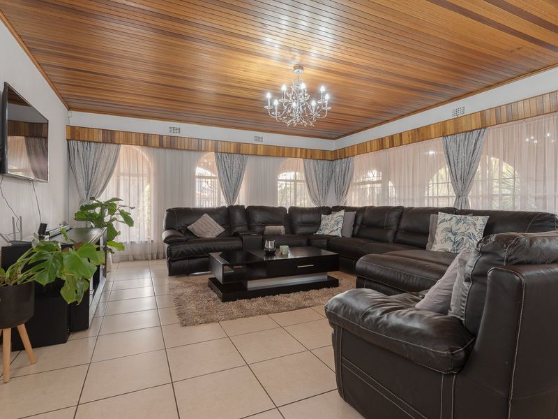 Spacious living room featuring a distinctive timber-clad ceiling, tiled flooring, and large arched windows that provide ample natural light.