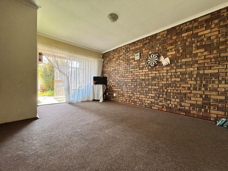 A living room featuring an exposed brick wall, neutral carpeting, and a sliding glass door providing access to the outdoor area.