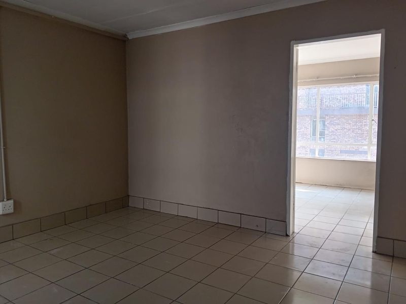 An empty living area featuring neutral ceramic floor tiles, coved ceilings, and a doorway leading to an adjacent sunroom or balcony space.