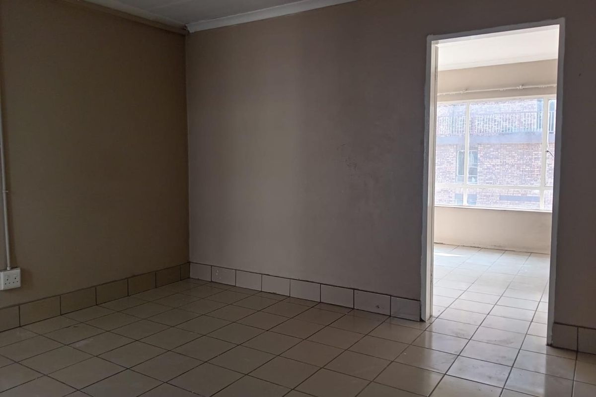 An empty living area featuring neutral ceramic floor tiles, coved ceilings, and a doorway leading to an adjacent sunroom or balcony space.