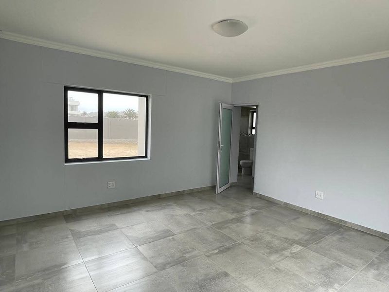A clean, empty bedroom featuring modern grey floor tiles, neutral walls, and an en-suite bathroom access point.