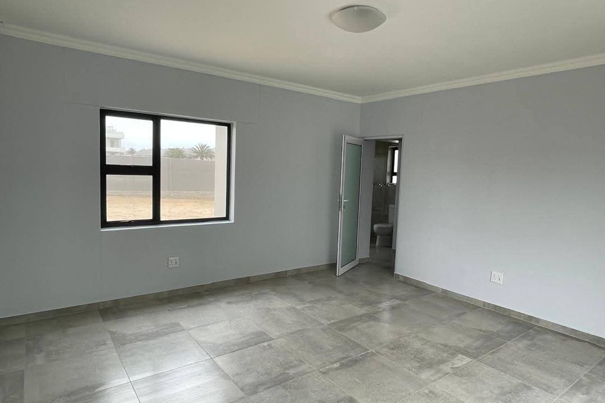 A clean, empty bedroom featuring modern grey floor tiles, neutral walls, and an en-suite bathroom access point.