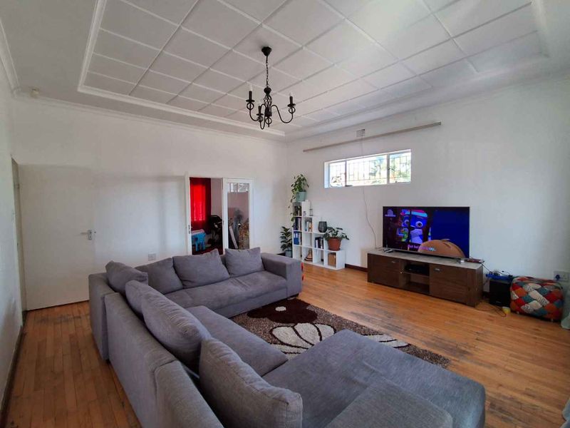 Spacious living room featuring original hardwood flooring, a decorative coffered ceiling, and a classic chandelier, offering a bright and versatile living space.
