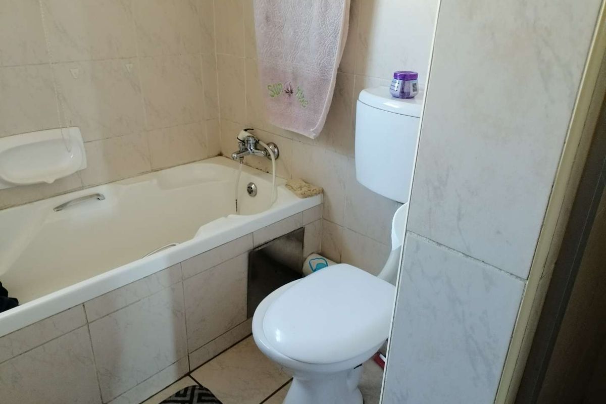 A functional bathroom featuring a built-in bathtub with shower mixer and a standard white ceramic toilet.