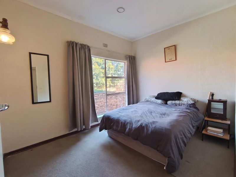A functional bedroom featuring carpeted flooring, a large window with security bars, and neutral wall finishes, providing a comfortable and well-lit living space.