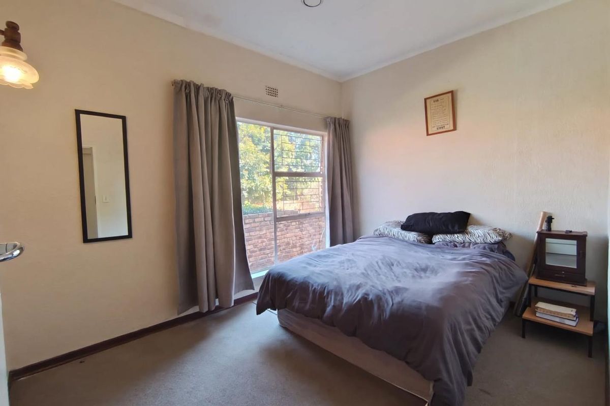 A functional bedroom featuring carpeted flooring, a large window with security bars, and neutral wall finishes, providing a comfortable and well-lit living space.