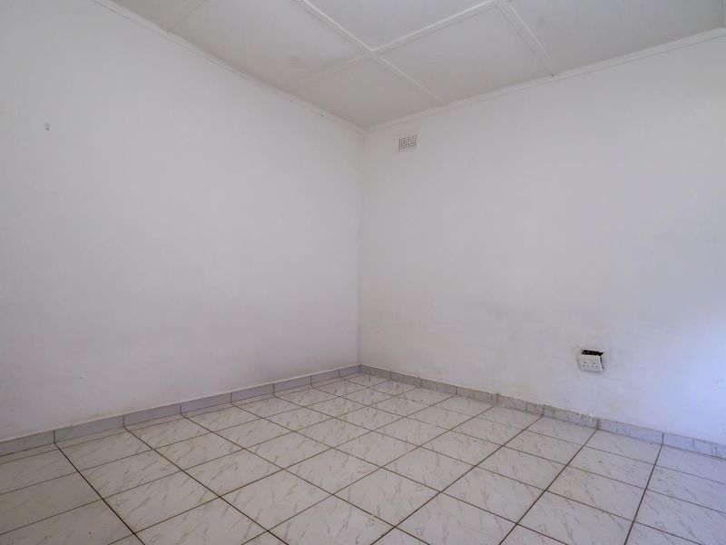 An empty bedroom featuring tiled flooring, a ceiling vent, and plain white walls, providing a blank canvas for potential interior design updates.