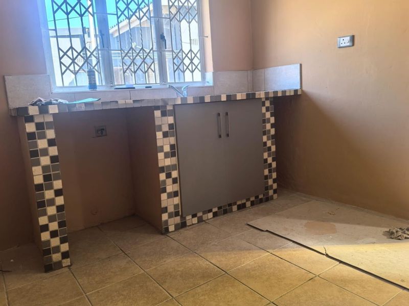 A basic kitchen area featuring a tiled countertop, built-in under-counter cabinetry, and a security gate over the window.