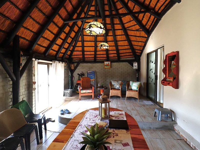 A rustic covered patio area featuring a traditional thatched roof with exposed timber rafters, sliding glass doors, and exposed brick walls.