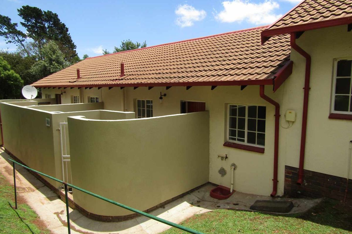 Rear exterior view of the retirement unit featuring a private courtyard area, tiled roof, and established garden surroundings.
