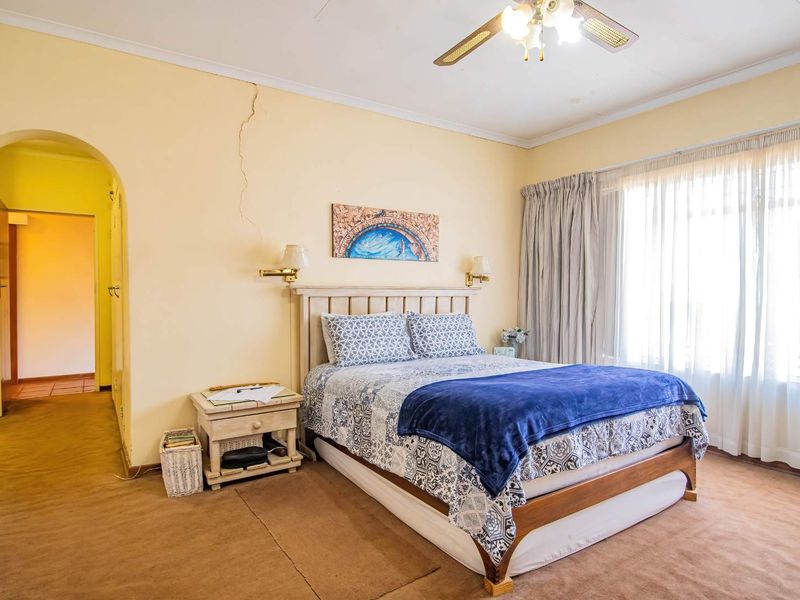 A bedroom featuring carpet flooring, a ceiling fan, and an arched entryway, showing a visible structural crack on the wall.