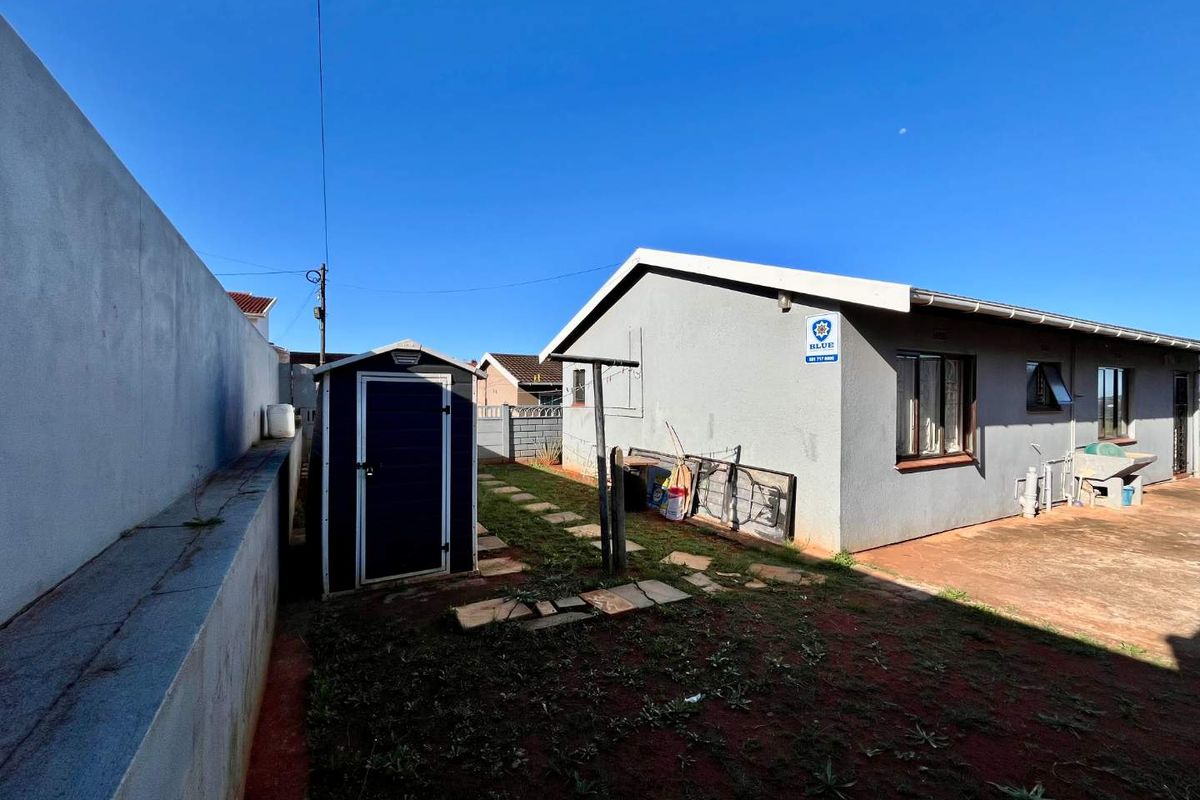 Rear exterior view of the property featuring a paved area, a storage shed, a washing line, and a boundary wall.