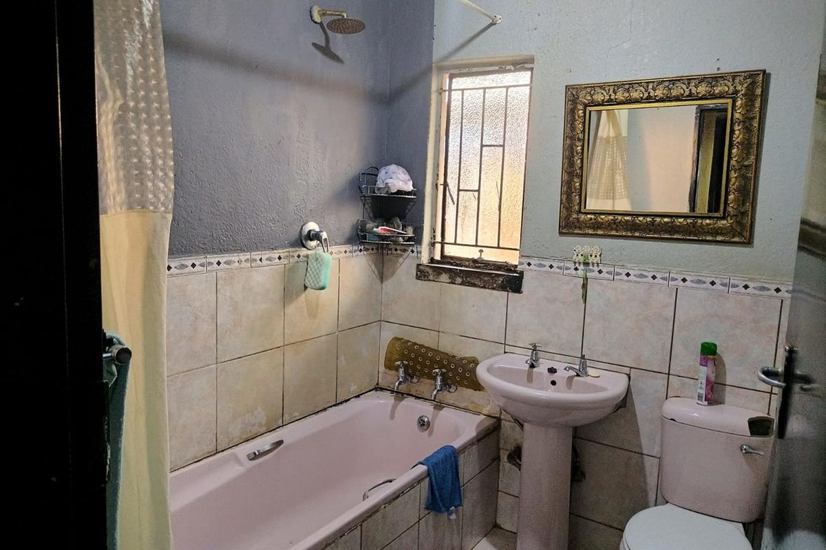 A dated bathroom featuring a pink pedestal basin, matching bathtub, toilet, and tiled splashback with security bars on the window.