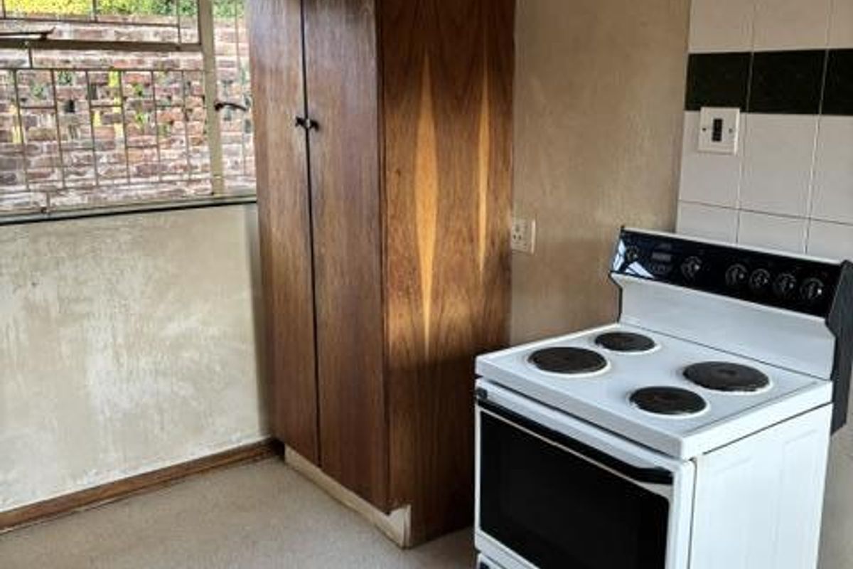 A basic kitchen area featuring a freestanding electric stove and a built-in wooden storage cabinet, requiring significant cosmetic updates and renovation.