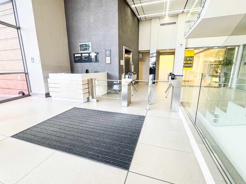 Modern commercial building lobby featuring a reception desk, secure turnstile access, elevator access, and high-quality tiled flooring with glass architectural elements.