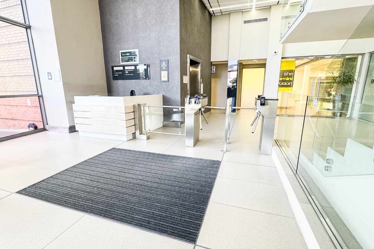 Modern commercial building lobby featuring a reception desk, secure turnstile access, elevator access, and high-quality tiled flooring with glass architectural elements.