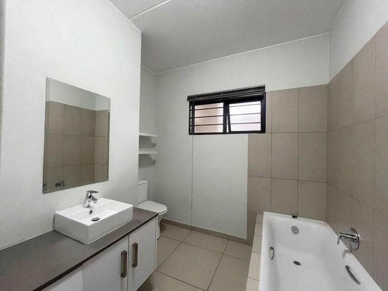 A clean, modern bathroom featuring a vessel sink vanity, bathtub, and neutral wall tiling, offering a functional and well-maintained space.