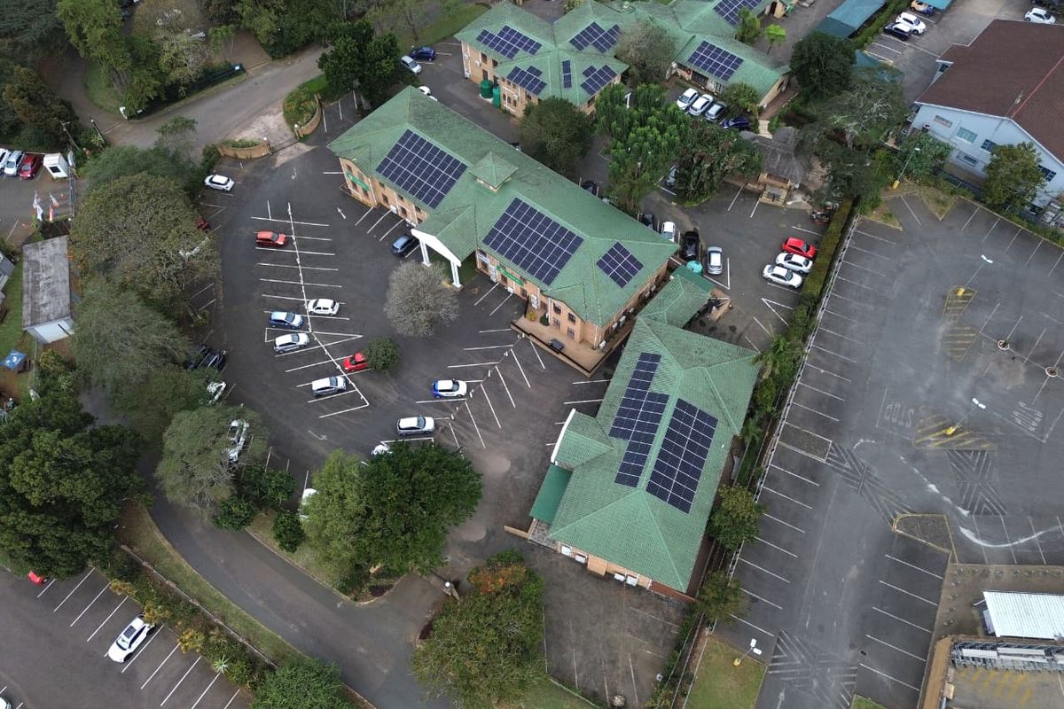 Aerial view of an office complex featuring multiple buildings with green tiled roofs, extensive solar panel installations, and ample paved parking facilities.
