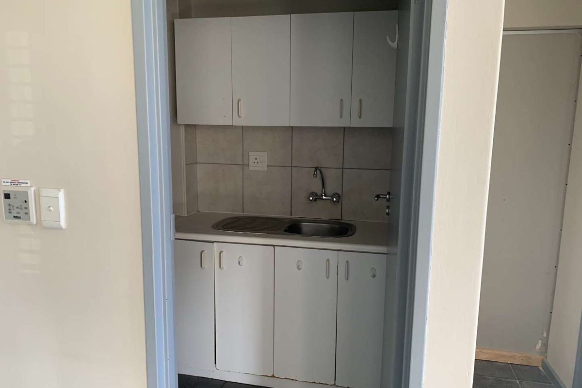A compact kitchenette area featuring white cabinetry, a stainless steel sink with faucet, and tiled splashback, suitable for office utility use.