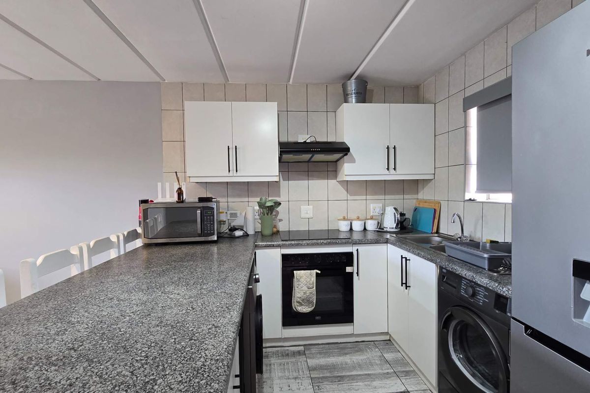 A functional kitchen featuring granite countertops, built-in oven, electric hob, extractor fan, and ample cabinetry with a tiled backsplash and flooring.