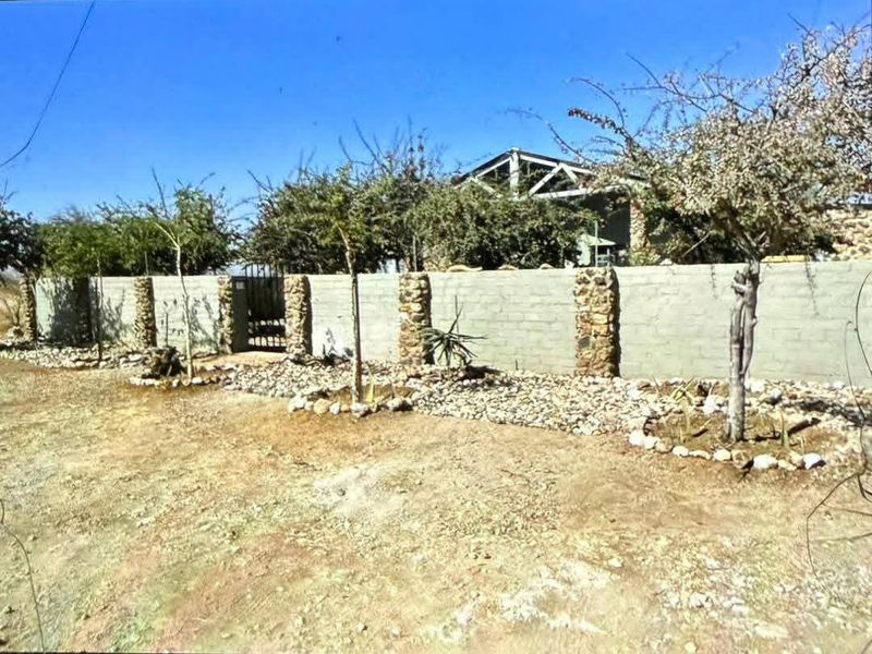 Front view of the property featuring a concrete block boundary wall with decorative stone-clad pillars and a metal entrance gate.