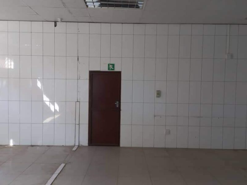An empty industrial utility space featuring white tiled walls, tiled flooring, and a functional emergency exit door.
