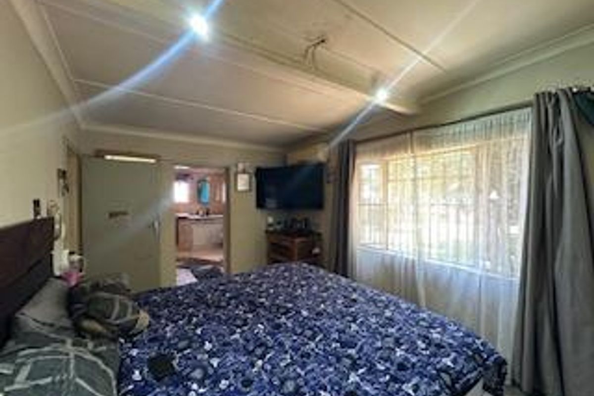 A bedroom featuring large windows with security bars, recessed ceiling lighting, and an adjoining bathroom area.