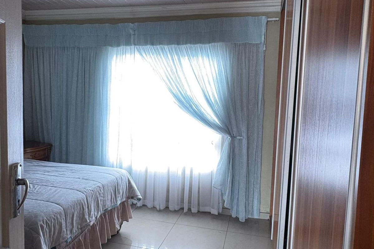 A bedroom featuring tiled flooring, built-in cupboards, and a tongue and groove ceiling with natural light filtering through window curtains.