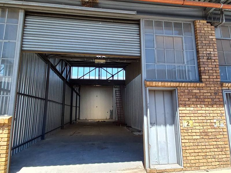Industrial unit exterior featuring a large roller shutter door, face brick facade, steel-framed windows, and essential fire safety equipment.