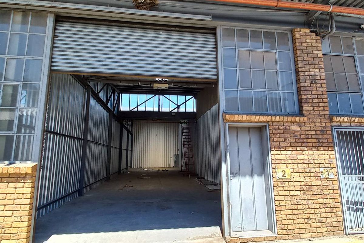 Industrial unit exterior featuring a large roller shutter door, face brick facade, steel-framed windows, and essential fire safety equipment.