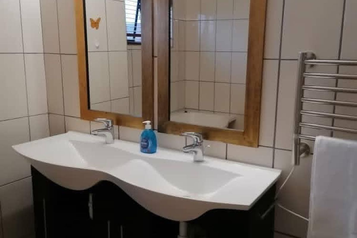 A bathroom featuring a double vanity with integrated basins, dual framed mirrors, wall-mounted towel warmer, and full-height wall tiling.