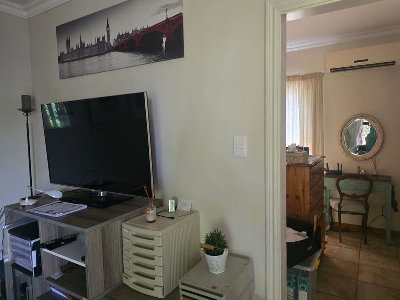 A living area featuring crown molding and tiled flooring, with a view into an adjacent room equipped with a wall-mounted air conditioning unit.