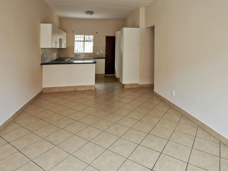 An open-plan living and kitchen area featuring neutral tiled flooring, built-in cabinetry, and a functional kitchen layout with a breakfast counter.