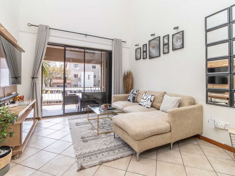 A bright living room featuring high ceilings, tiled flooring, and a large sliding glass door providing access to an outdoor balcony area.