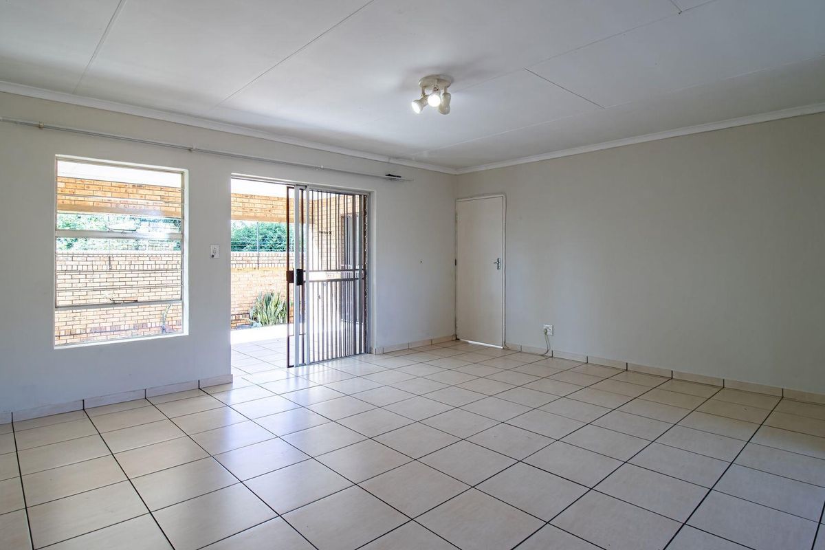 Spacious open-plan living area featuring neutral tiled flooring, large windows, and direct access to a covered patio through a security sliding door.