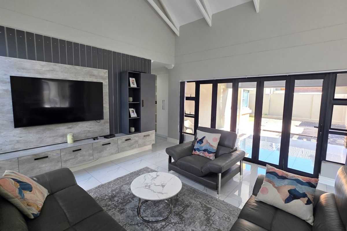 Modern living room featuring high vaulted ceilings, built-in media cabinetry, and large black-framed folding doors opening to the pool area.