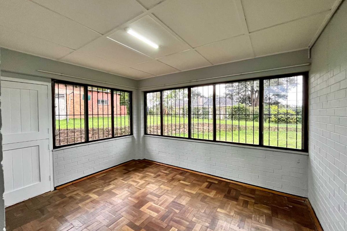 An empty living room featuring parquet flooring, painted brick walls, and large windows with security bars, offering a bright and versatile space.
