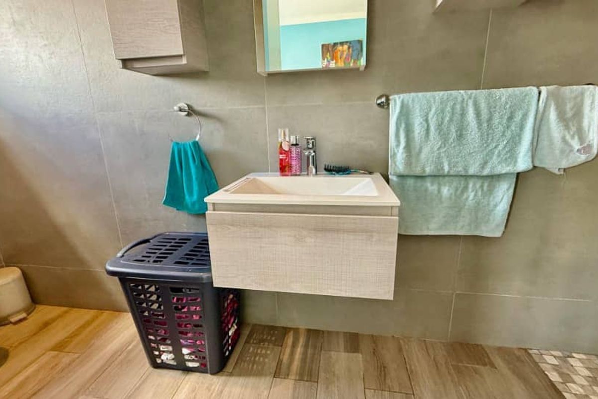 A modern bathroom featuring a wall-mounted vanity with a basin, large format wall tiles, and wood-look floor tiling.