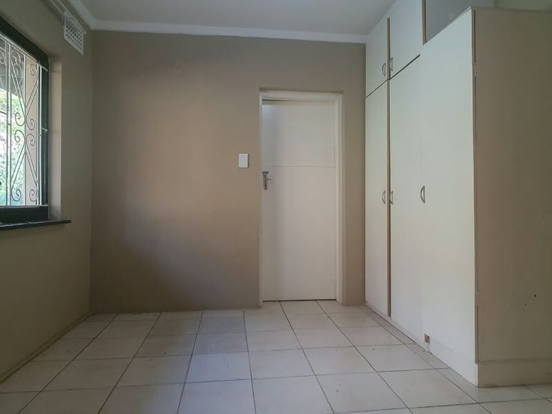 A vacant bedroom featuring tiled flooring, built-in cupboards, and a window fitted with security burglar bars.