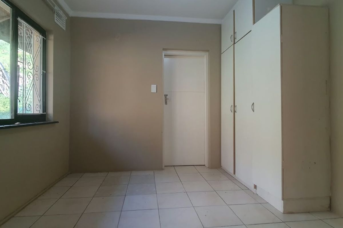 A vacant bedroom featuring tiled flooring, built-in cupboards, and a window fitted with security burglar bars.